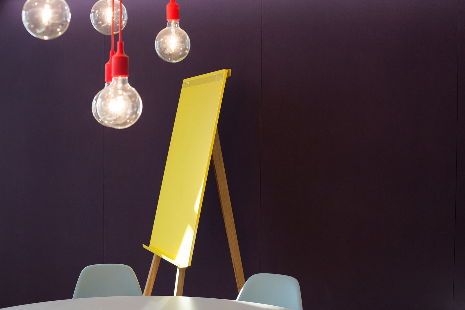 ein gelbes Flipchart mit Beinen aus Eichenholz vor einer lila Wand, ein Lichtreflex auf der gelben Fläche